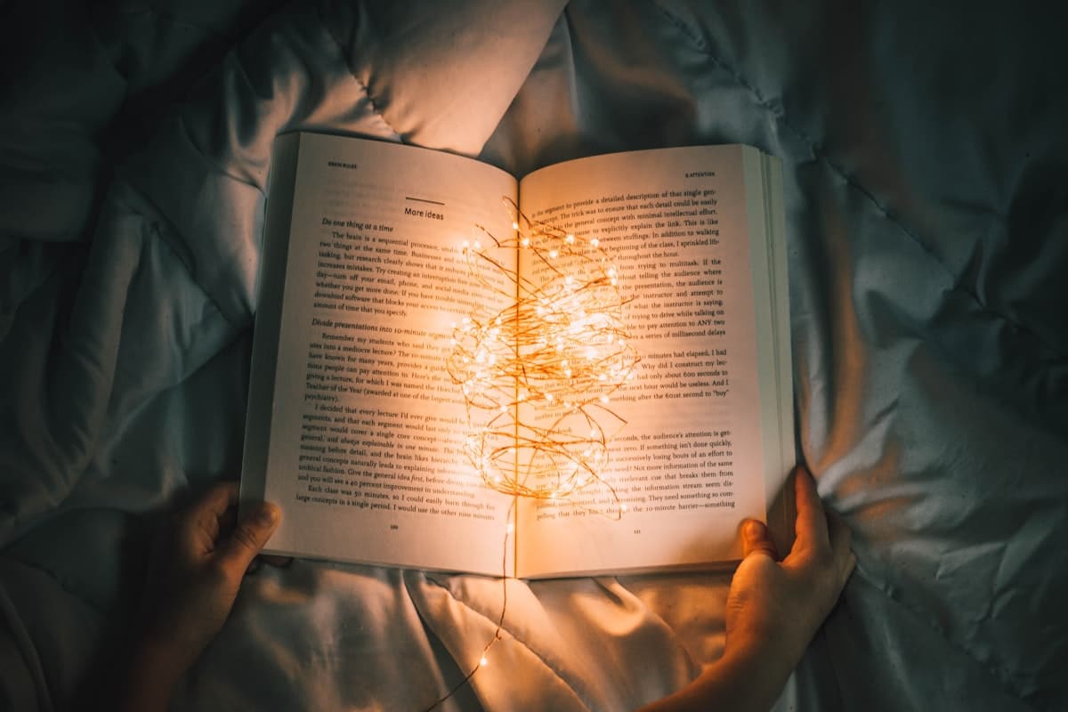 An open book on a bed, lit by a string of small warm lights